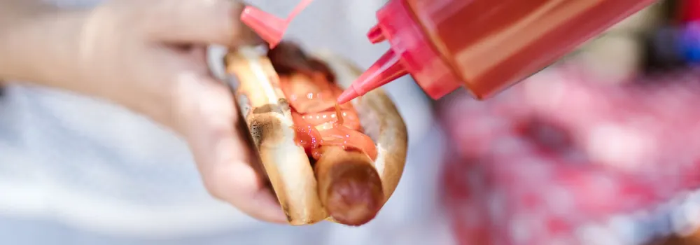 Punasest kastmepudelist voolab ketšup käes hoitud hotdogi vorstile